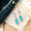 The feminine turquoise petal post earrings styled on wood with linen, blue velvet, and dried grass