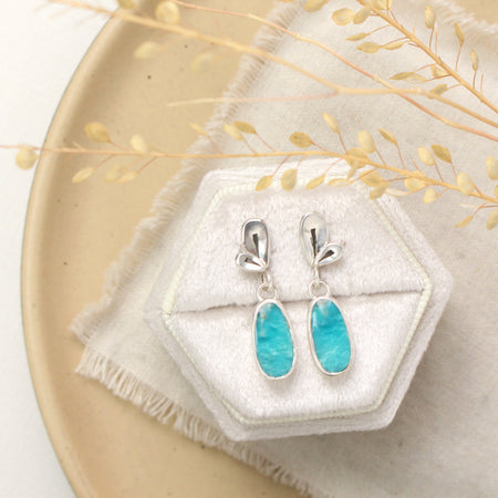 The feminine petal post earrings styled on a white velvet box with linen and dried grass