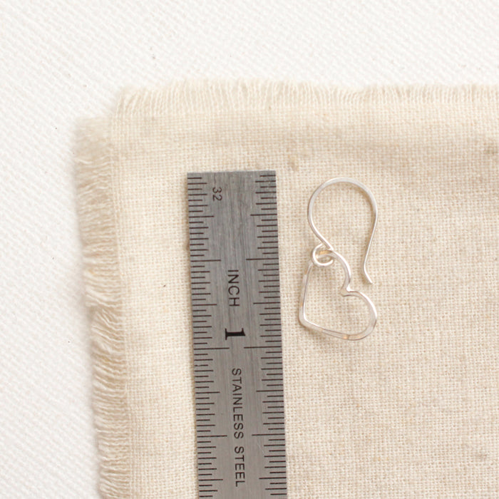 A floating silver heart earring next to a ruler for size reference