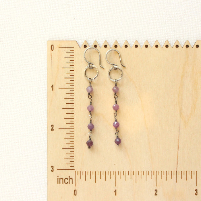 The flowing ruby hoop earrings on a wooden ruler for size reference