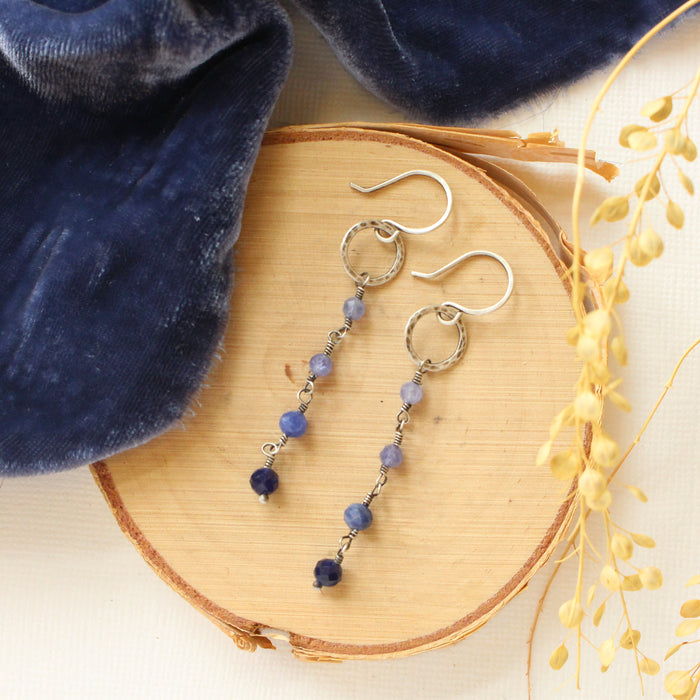 The flowing vinca mini hoop earrings styled on wood with blue velvet and dried grass