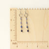The flowing vinca mini hoop earrings on a wooden ruler for size reference
