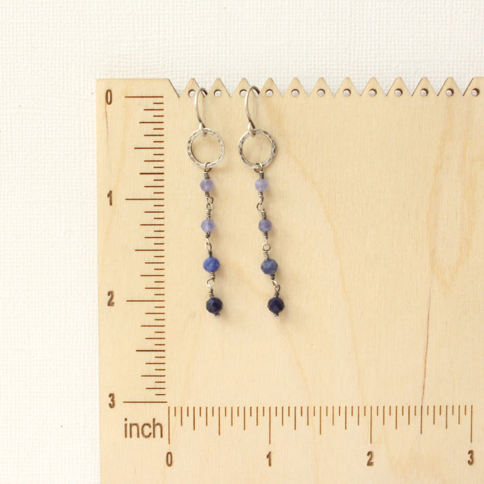 The flowing vinca mini hoop earrings on a wooden ruler for size reference