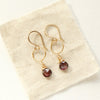 The rhodolite garnet gold hoop earrings styled on tan linen.