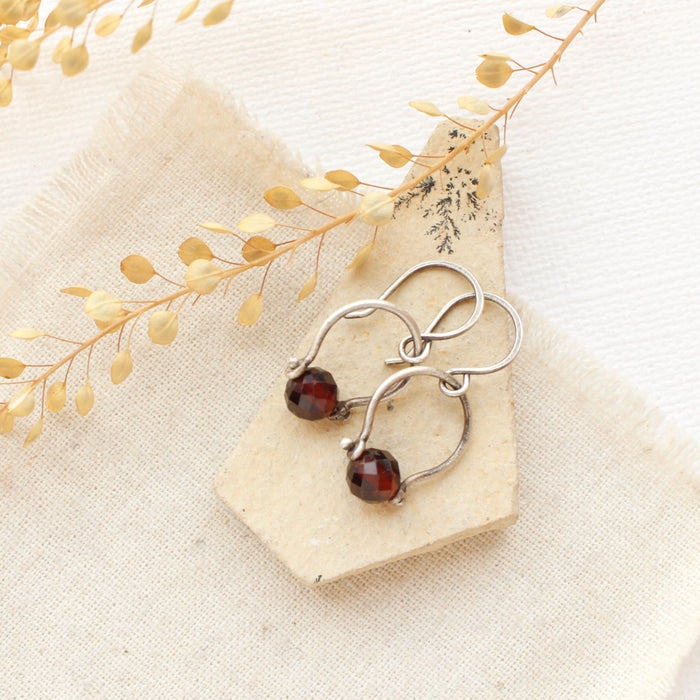 The garnet la cloche earrings styled on a tan rock with linen and dried grass
