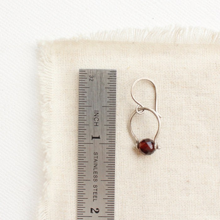 A garnet la cloche earring next to a ruler for size reference