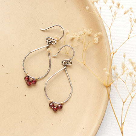 The garnet wrapped teardrop hoop earrings styled on a tan plate with dried grass