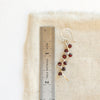A garnet wrapped silver vine earring next to a ruler for size reference