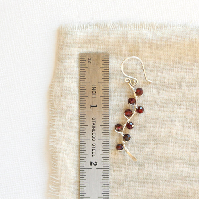 A garnet wrapped silver vine earring next to a ruler for size reference