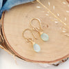 The gold chalcedony drop earrings styled on wood with blue velvet and dried grass
