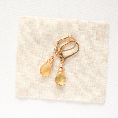 The gold citrine drop earrings styled on tan linen
