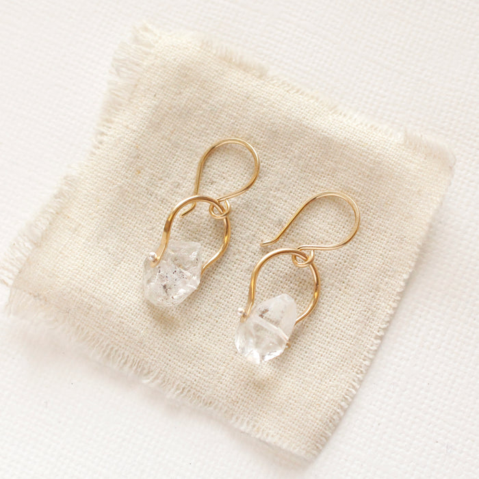 The gold herkimer diamond la cloche earrings styled on tan linen
