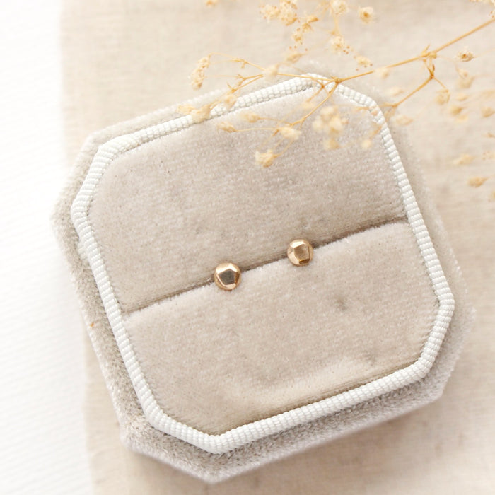 The gold nugget post earrings styled on a tan velvet box with dried grass