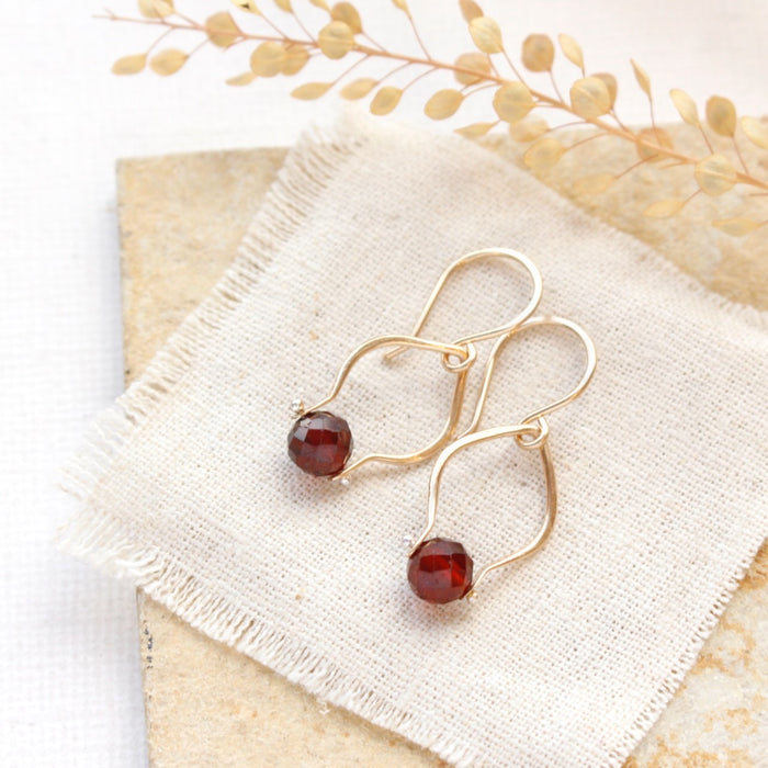 The garnet delhi earrings styled on a tan rock with linen and dried grass