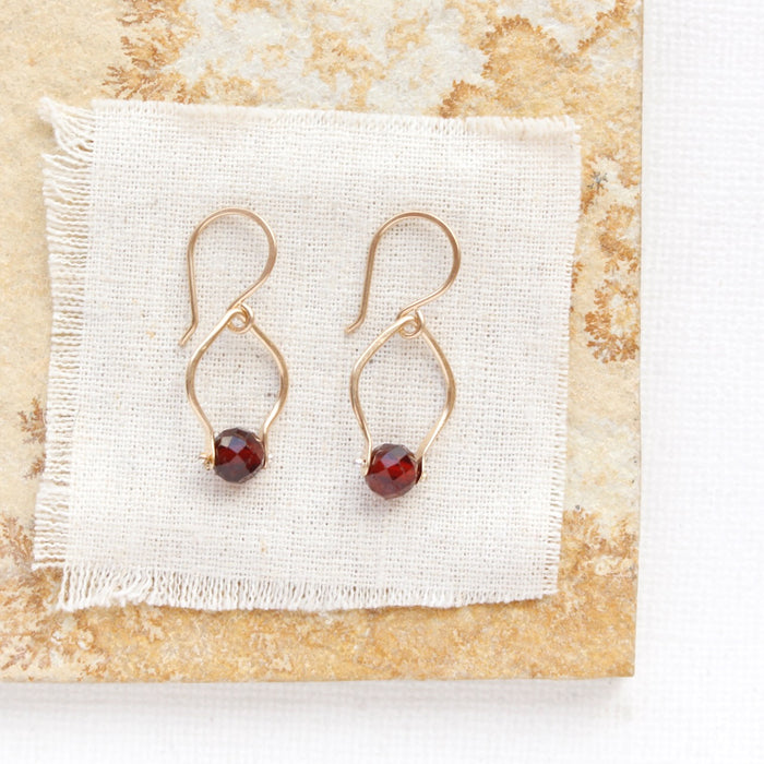 The garnet delhi earrings styled on a tan rock and tan linen