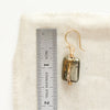 A gold wrapped pyrite earring next to a ruler for size reference