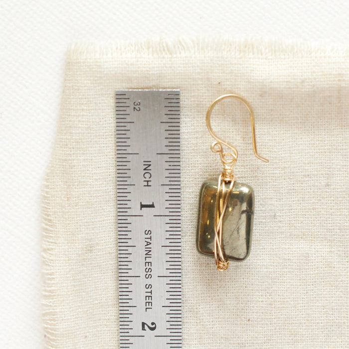 A gold wrapped pyrite earring next to a ruler for size reference