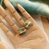 The gold wrapped turquoise post earrings styled on a wooden hand with green velvet and linen
