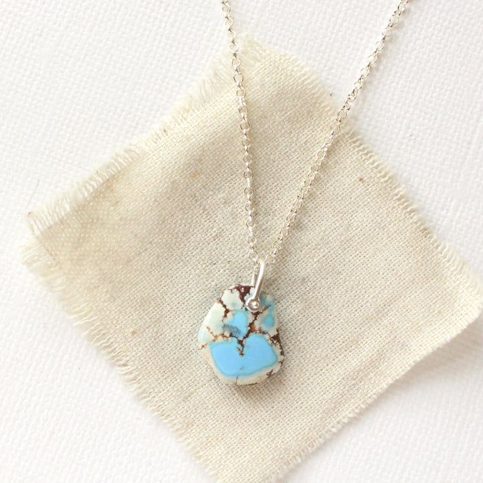 The back of the golden hills turquoise necklace styled on tan linen