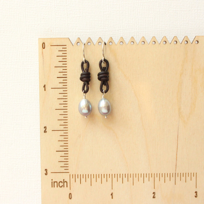 The gray pearl leather earrings on a wooden ruler for size reference