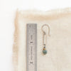A green apatite and brass hoop earring next to a ruler for size reference