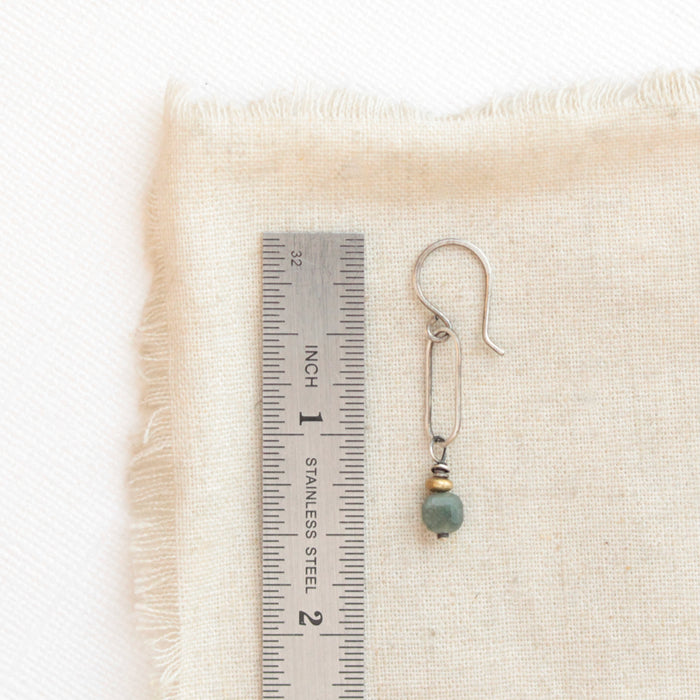 A green apatite and brass hoop earring next to a ruler for size reference