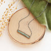 The green apatite bronze bar necklace styled on wood with green velvet and dried grass