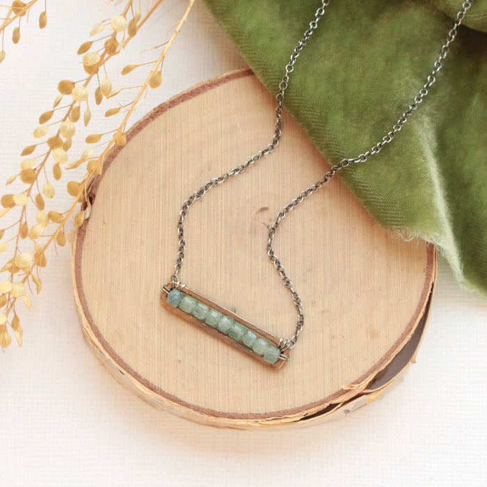 The green apatite bronze bar necklace styled on wood with green velvet and dried grass