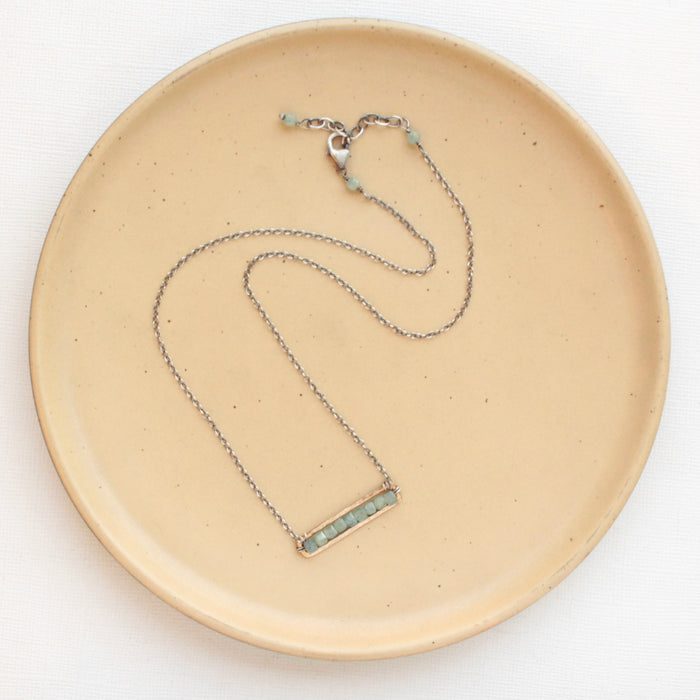 The green apatite bronze bar necklace styled on a tan plate to show the adjustable lobster clasp closure