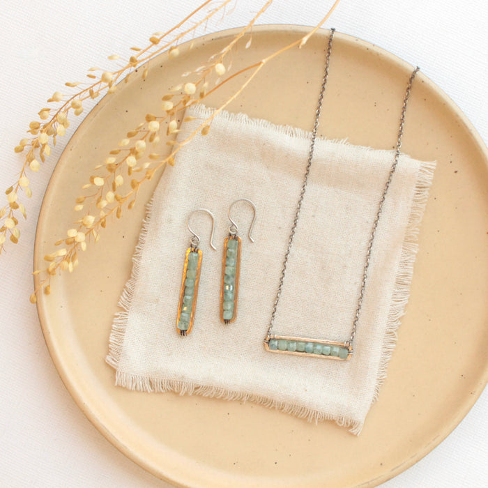 The green apatite bronze bar necklace styled on a tan plate with the matching earrings 