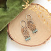 The bronze wanderer arch green apatite earrings styled on wood with green velvet and dried grass