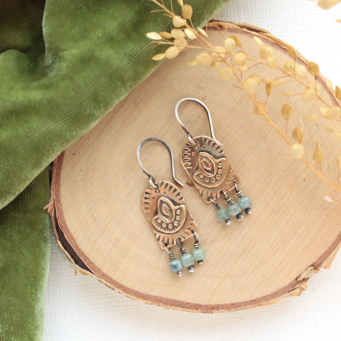 The bronze wanderer arch green apatite earrings styled on wood with green velvet and dried grass