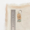 A bronze wanderer arch green apatite earring next to a ruler for size reference