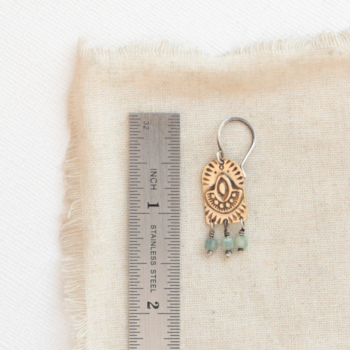 A bronze wanderer arch green apatite earring next to a ruler for size reference
