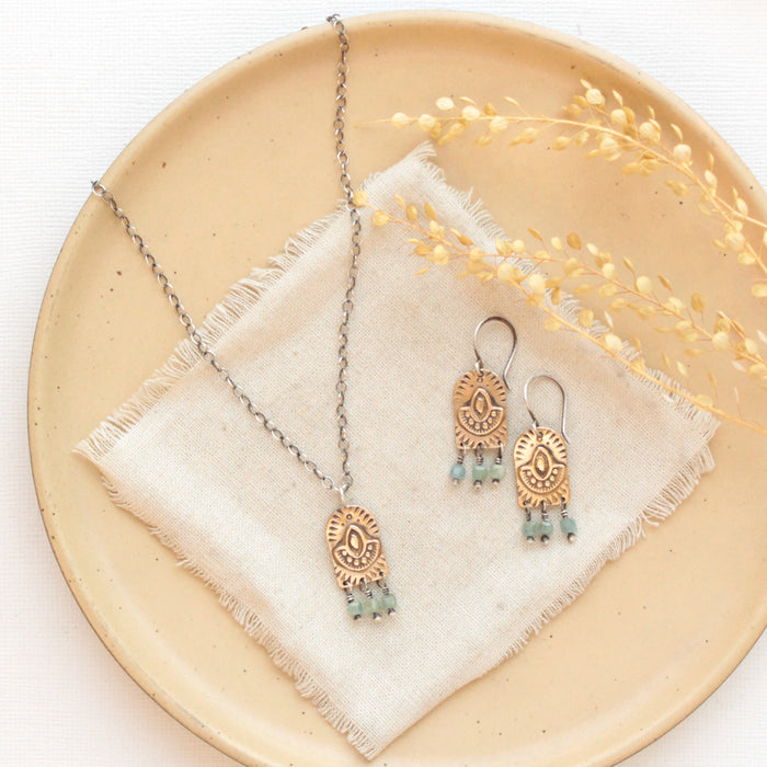 The bronze wanderer arch green apatite earrings styled on a tan plate with the matching necklace