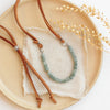 The apatite adjustable leather necklace styled on a tan plate with linen and dried grass
