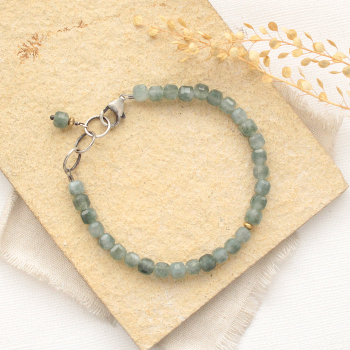 The green apatite cube bracelet styled on a tan rock with linen and dried grass