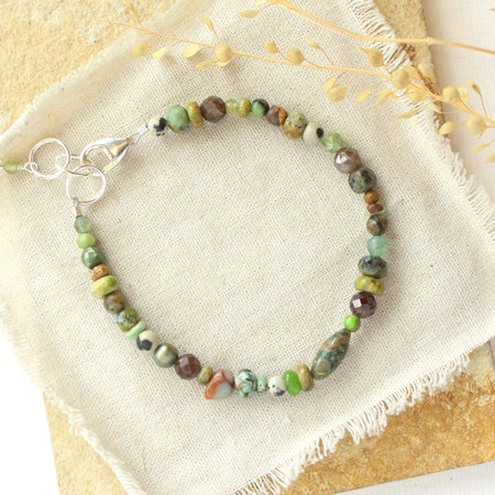 The green eyes gemstone bracelet styled on a tan rock with linen and dried grass