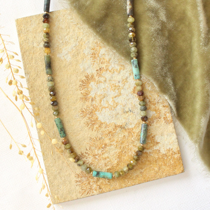 The beaded lana necklace styled on a tan rock with green velvet and dried grass