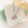 The green kyanite and sprout charm necklace styled on a green rock with tan linen and dried grass