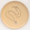 The green kyanite and sprout charm necklace styled on a tan plate to show the adjustable lobster clasp closure