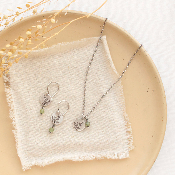 The green kyanite & sprout charm necklace styled with the matching earrings on a tan plate with linen and dred grass