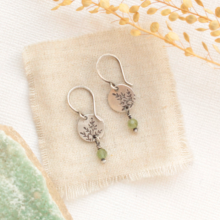 The green kyanite sprout earrings styled on tan linen with dried grass and a green rock