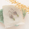 The green kyanite sprout earrings styled on a green rock with linen and dried grass