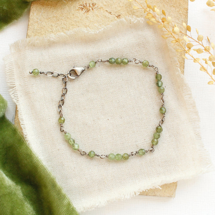 The wrapped green kyanite bracelet styled on a tan rock with linen, green velvet and dried grass