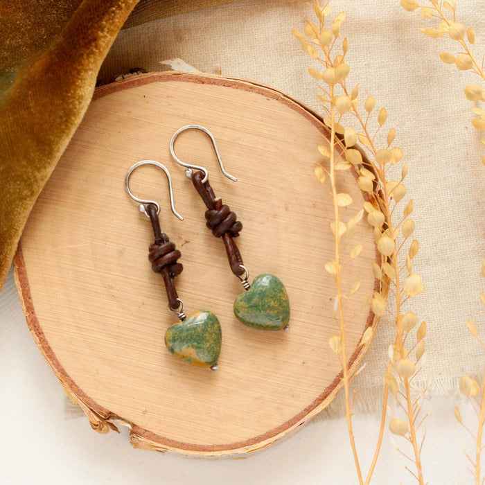 The turquoise heart leather earrings styled on wood with yellow velvet and dried grass