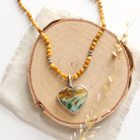 The green variscite heart and knotted mookaite necklace is styled on wood with linen and dried grass