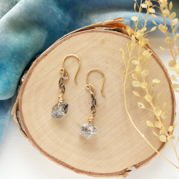 The herkimer diamond mixed metal earrings styled on wood with blue velvet and dried grass