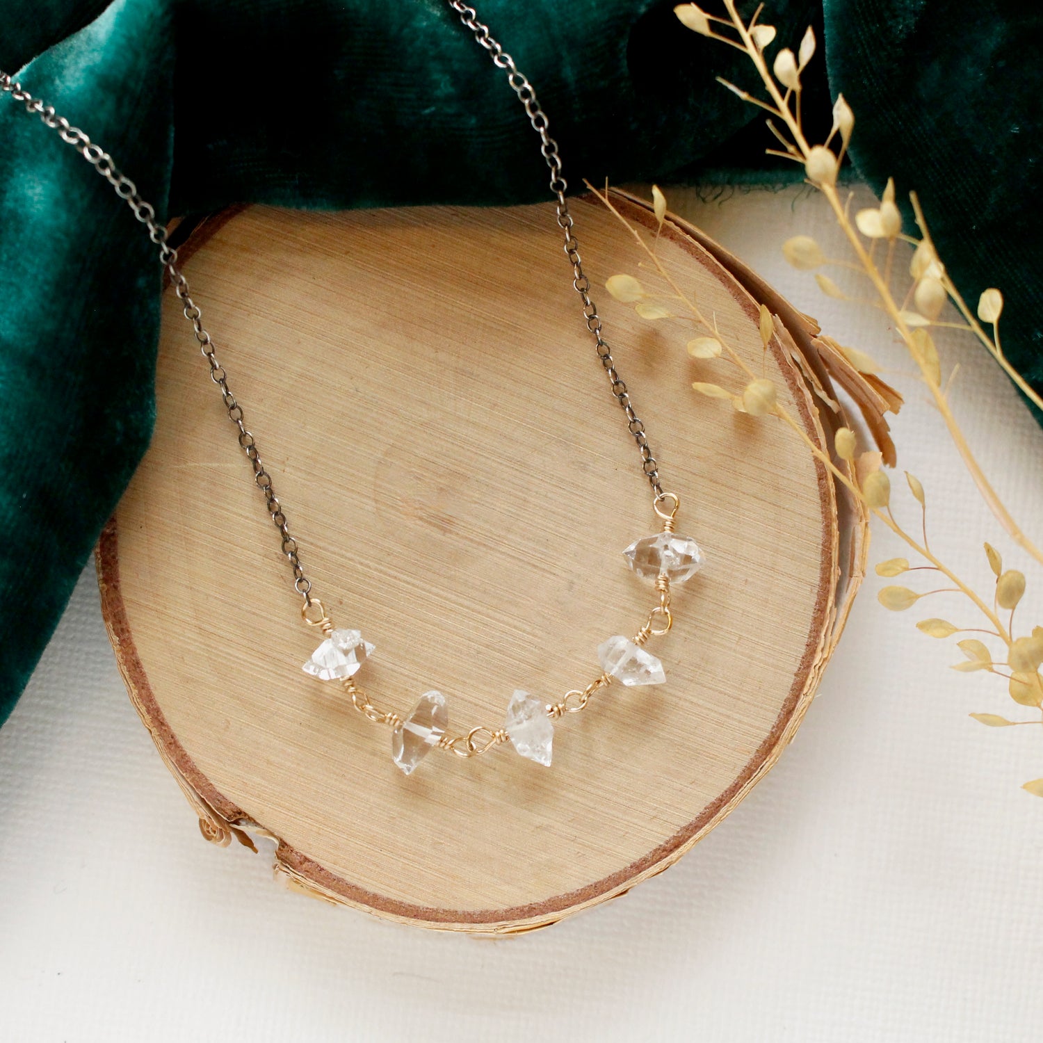 The mixed metal herkimer diamond necklace styled on wood with green velvet and dried grass