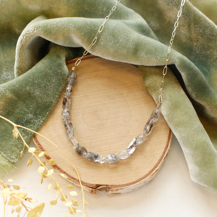 The herkimer diamond collar necklace styled on wood with green velvet and dried grass